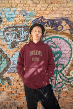 Person wearing a maroon hoodie with 'DREAMS EXPIRE' text against a graffiti-covered brick wall.