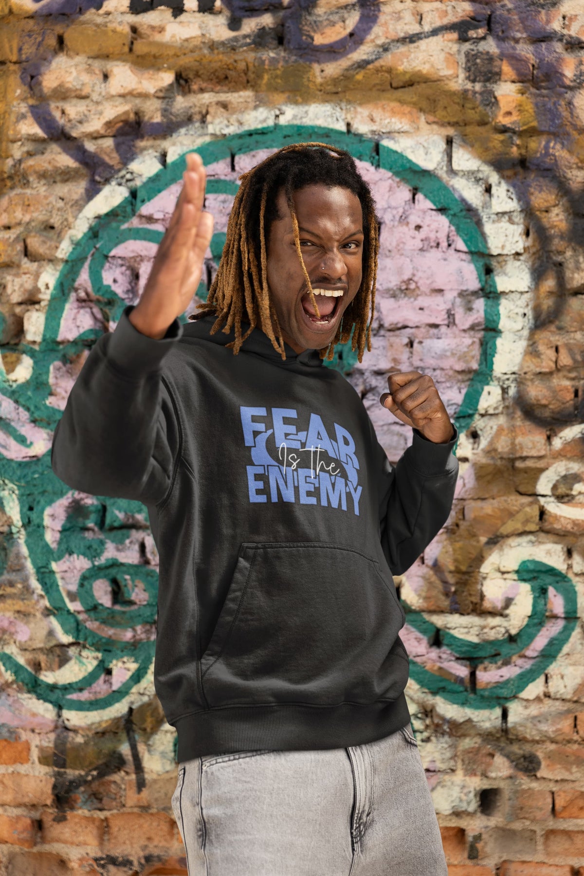 Person wearing a black hoodie with 'FEAR THE ENEMY' text in front of a graffiti-covered wall.