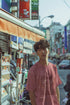 Person wearing a pink shirt standing on a street with shops and signs in the background
