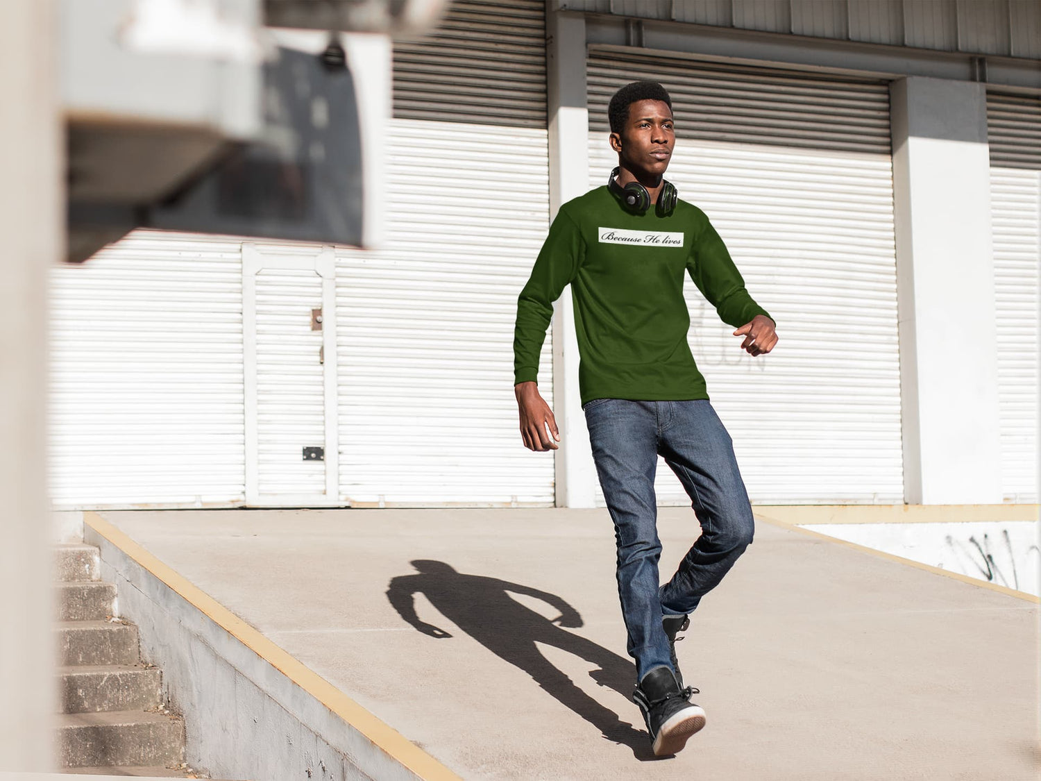 Man in a green sweater and jeans walking outdoors on a concrete surface.
