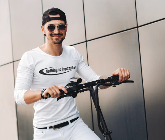 Man holding a scooter with 'Nothing is impossible' shirt against a tiled wall.