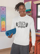 Person wearing a white sweatshirt with text holding a blue yoga mat in a room.