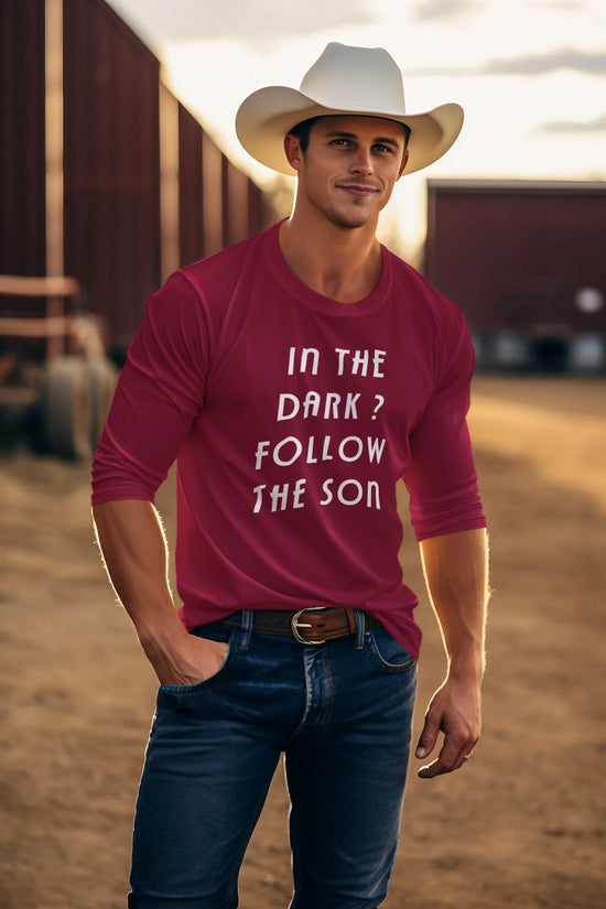 Man wearing a red t-shirt with text and a cowboy hat in a rural setting