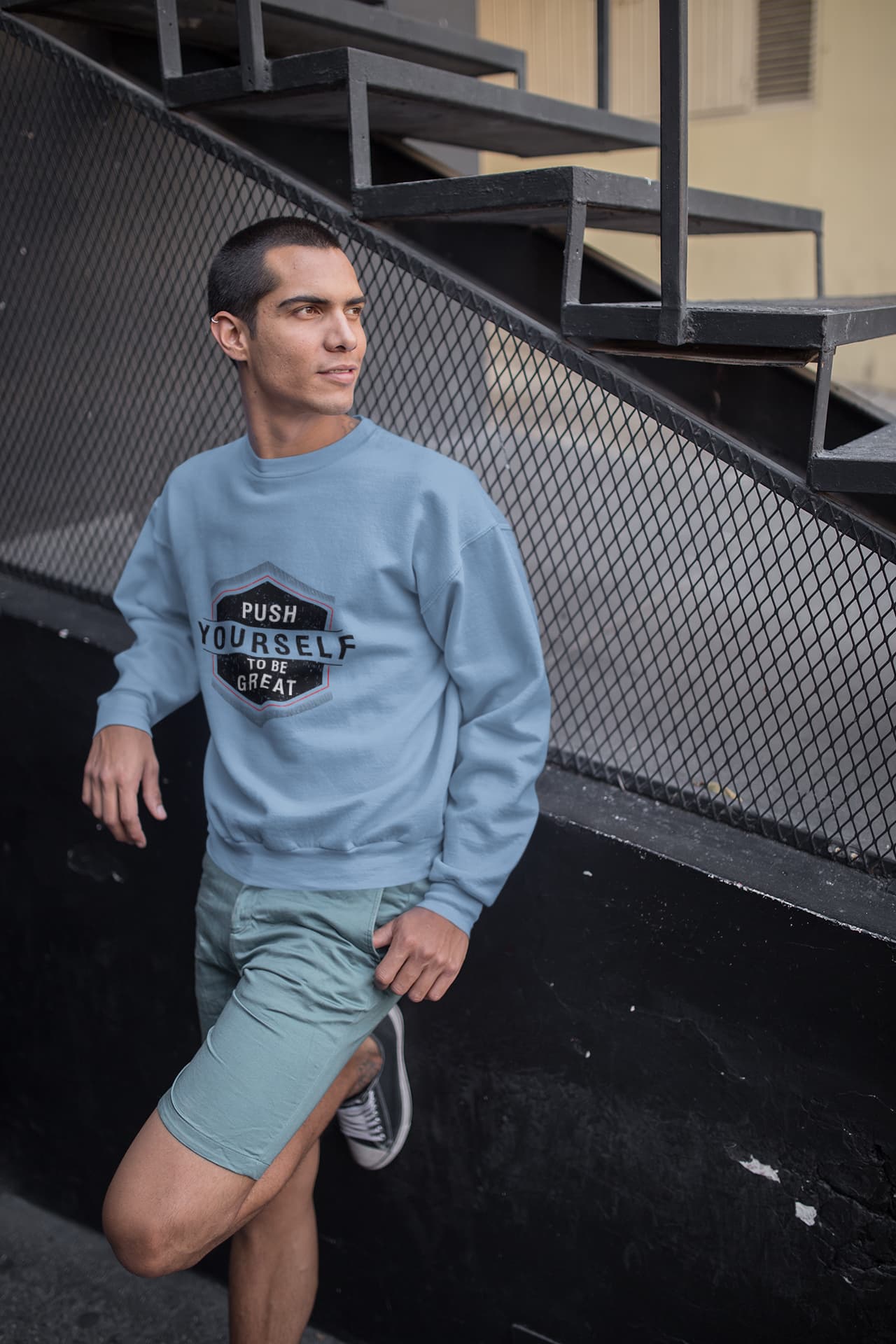 Person wearing a light blue sweatshirt with text and shorts, leaning against a metal staircase.