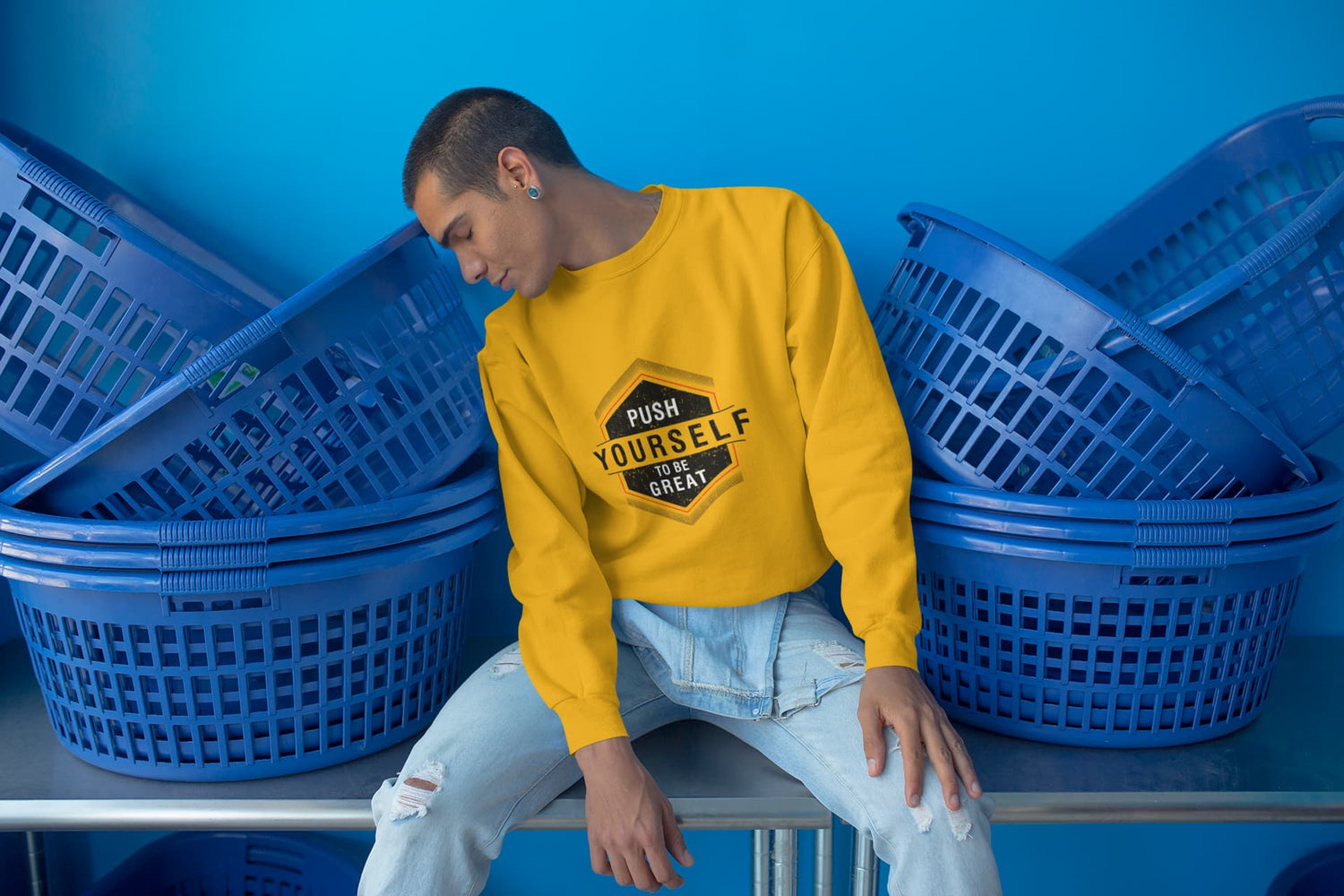 Person wearing a yellow sweatshirt with text sitting among blue laundry baskets.