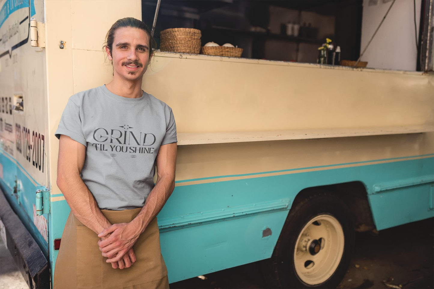 Man standing in front of a food truck wearing a t-shirt with 'The Grind Till You Shine' text.