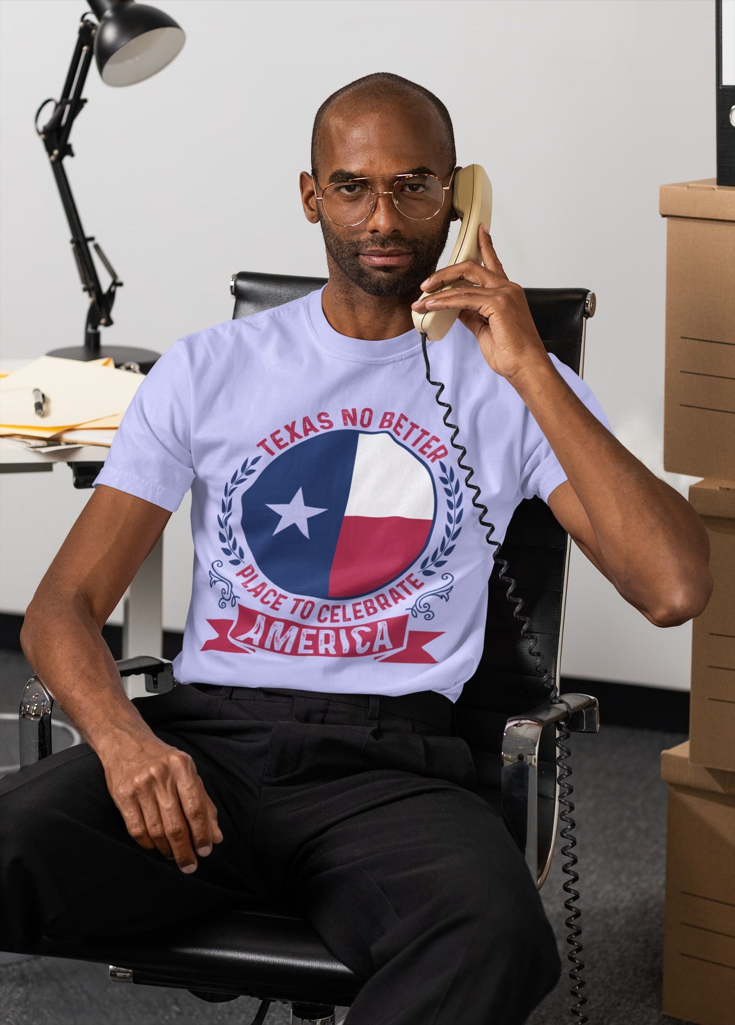 Man sitting in an office chair talking on a phone, wearing a t-shirt with a Texas-themed design.