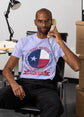 Man sitting in an office chair talking on a phone, wearing a t-shirt with a Texas-themed design.