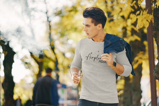 Man wearing a gray sweatshirt with text, holding a drink outdoors with trees in the background