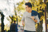 Man wearing a gray sweatshirt with text, holding a drink outdoors with trees in the background