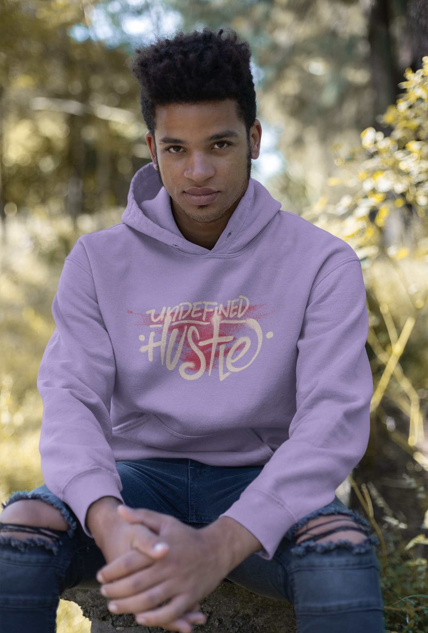 Person wearing a purple hoodie with text sitting in a natural setting