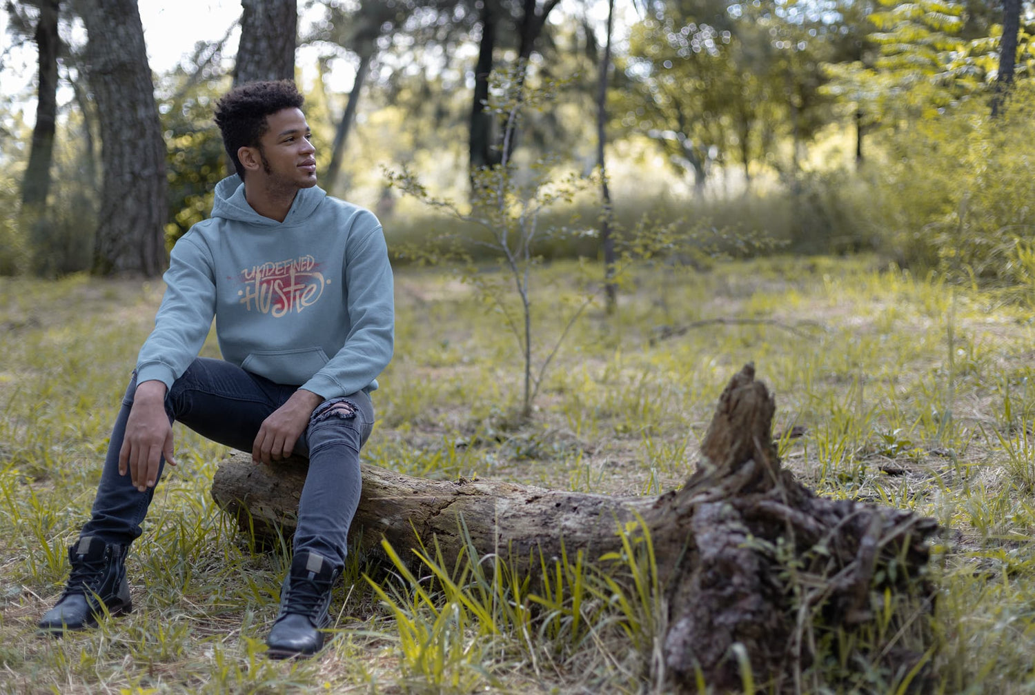 Person sitting on a log in a forest wearing a hoodie with text.