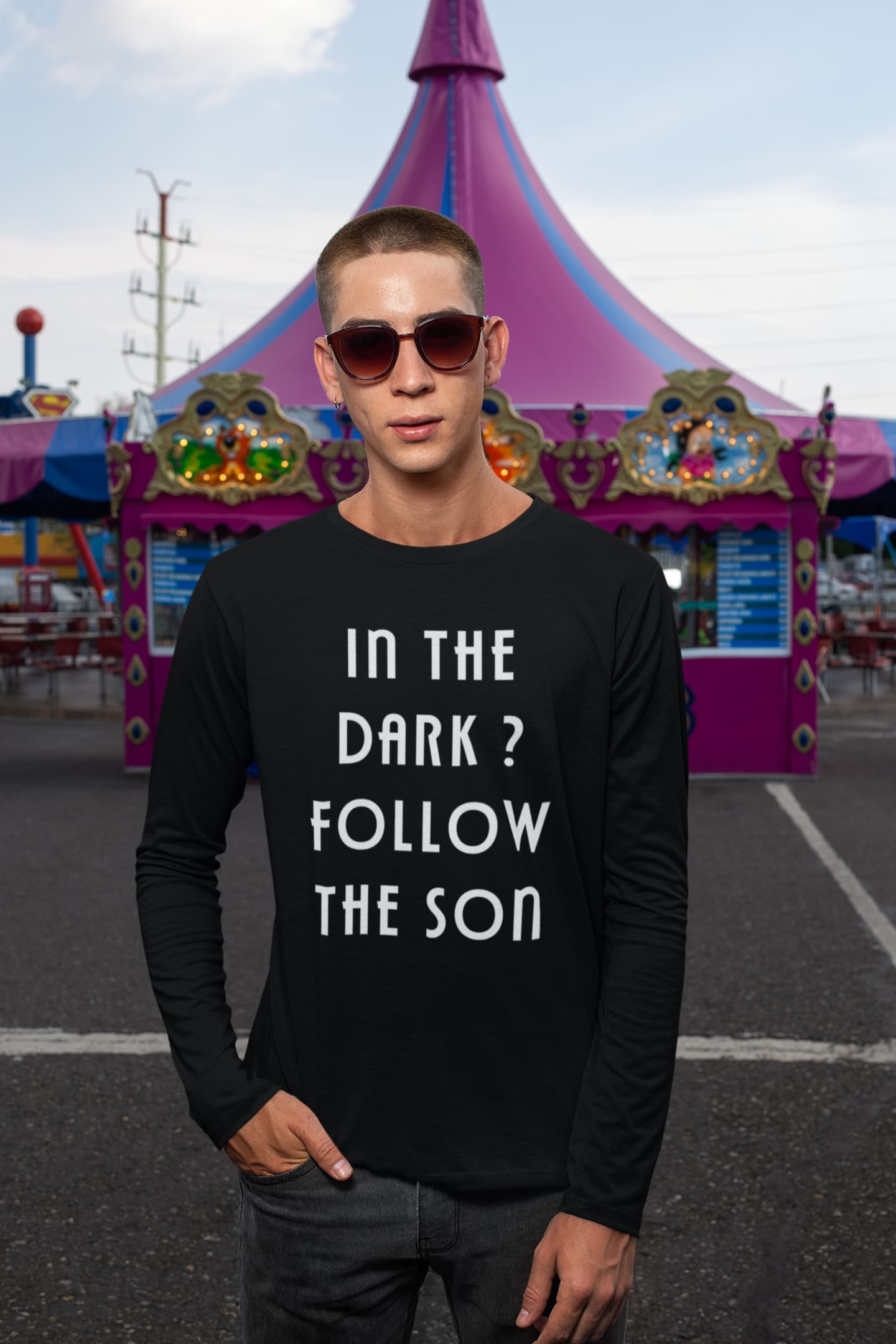 Person wearing a black long-sleeve shirt with text in front of a colorful tent at a fair.