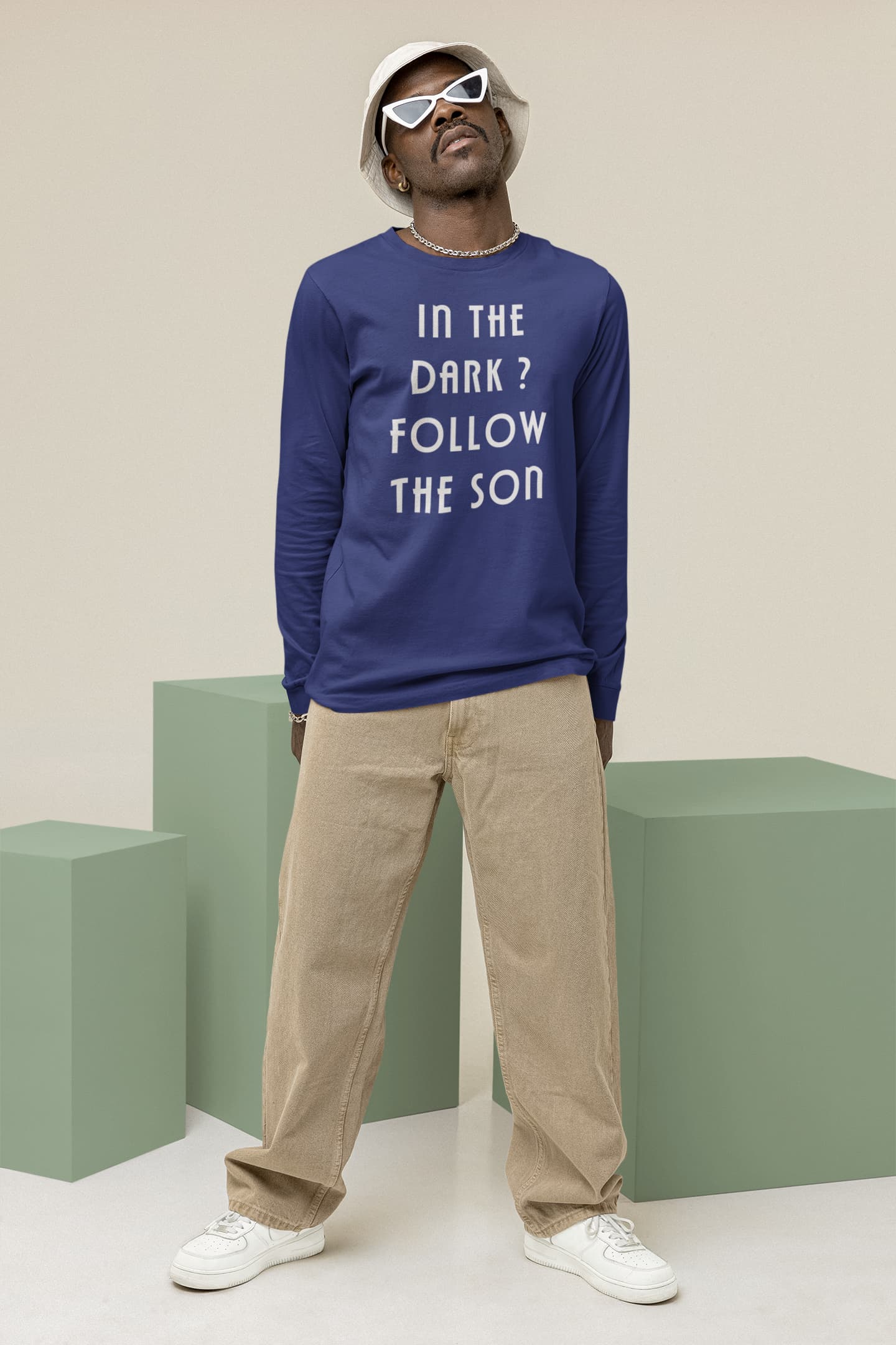 Man wearing a blue sweatshirt with text, beige pants, and white sneakers on a plain background