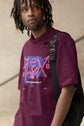 Person wearing a purple t-shirt with a graphic design, standing against a neutral background
