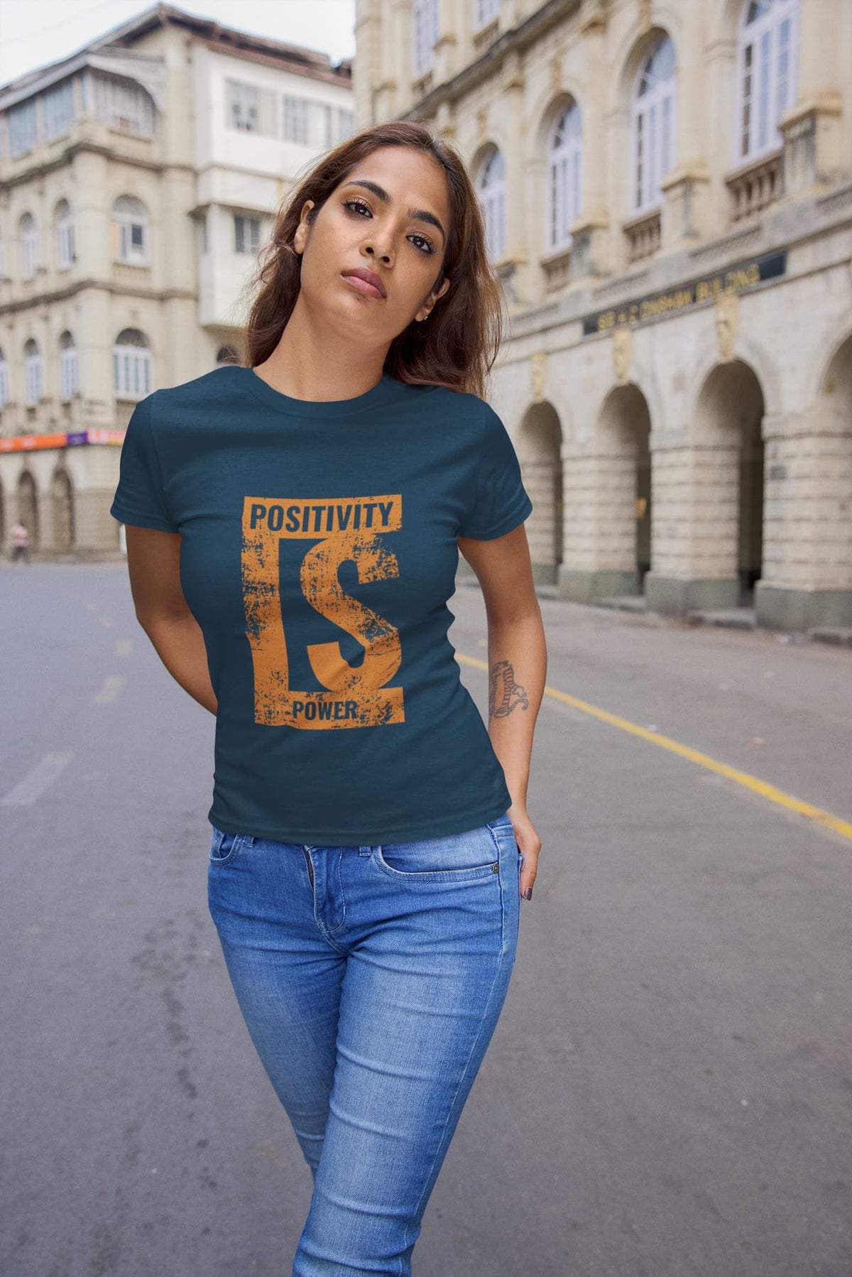 Woman wearing a blue t-shirt with 'Positivity is Power' design on a street.