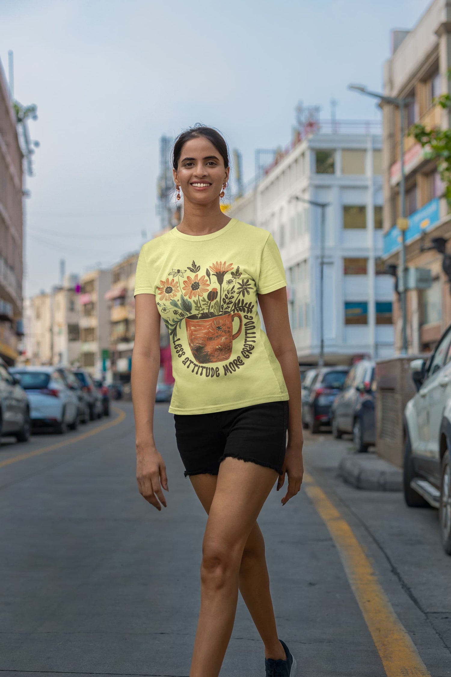 Woman wearing a yellow t-shirt with a graphic design on a city street.