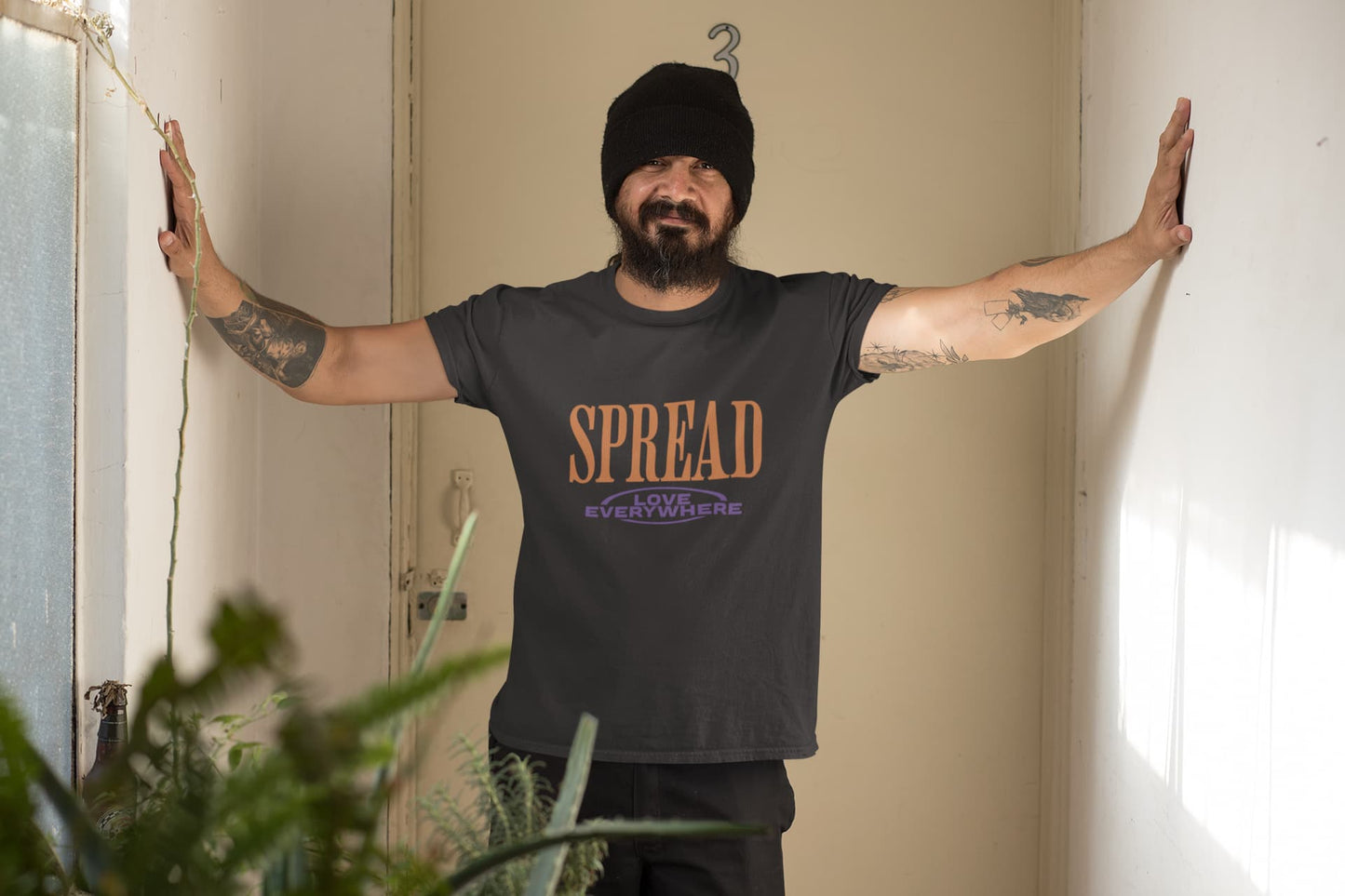Person wearing a black t-shirt with 'SPREAD' text in a room with plants.