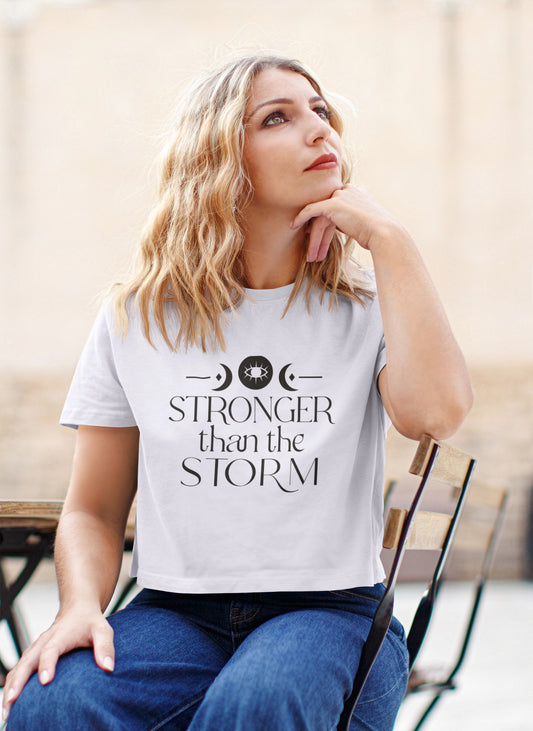 Woman wearing a white t-shirt with 'Stronger than the Storm' text, sitting outdoors.