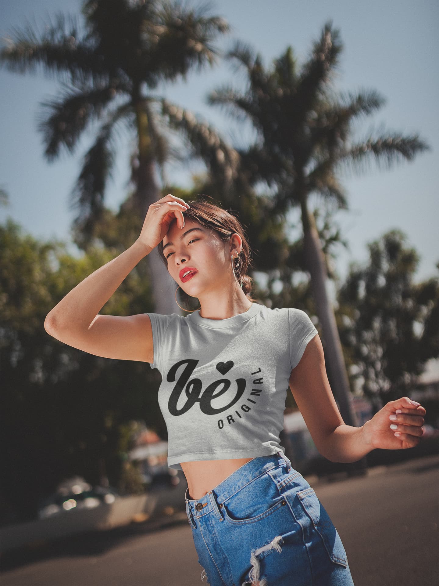 Woman wearing a white t-shirt with text and blue jeans standing outdoors with palm trees in the background