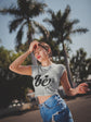 Woman wearing a white t-shirt with text and blue jeans standing outdoors with palm trees in the background