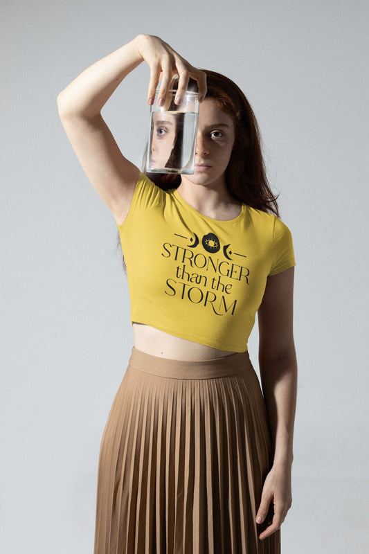 Woman wearing a yellow crop top with 'Stronger than the storm' text, holding a glass jar.