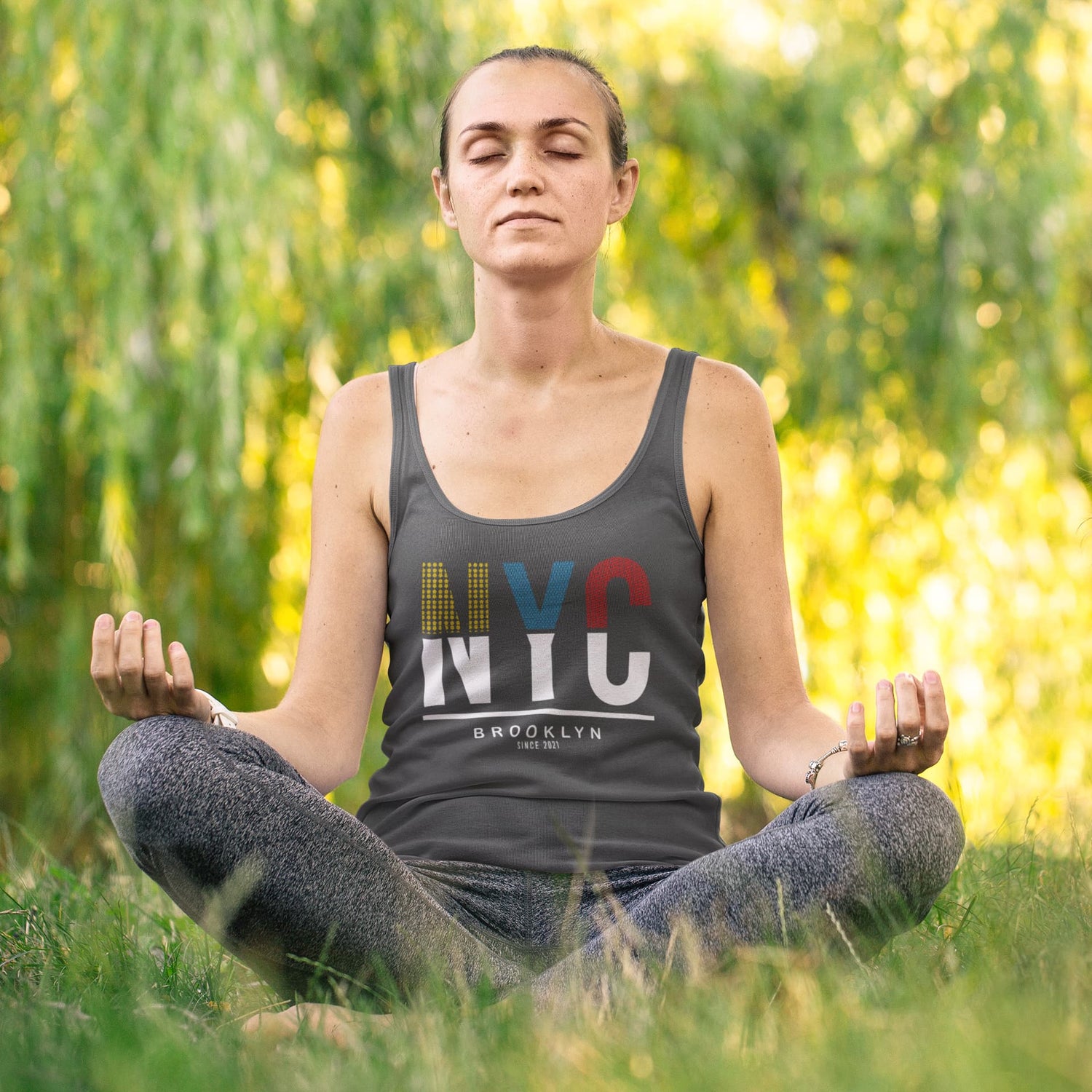 Woman meditating outdoors wearing an NYC tank top.