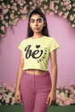 Woman wearing a light yellow t-shirt with text and pink pants against a floral background