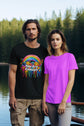 Two people standing by a lake with one wearing a black t-shirt with a colorful design and the other wearing a purple t-shirt.