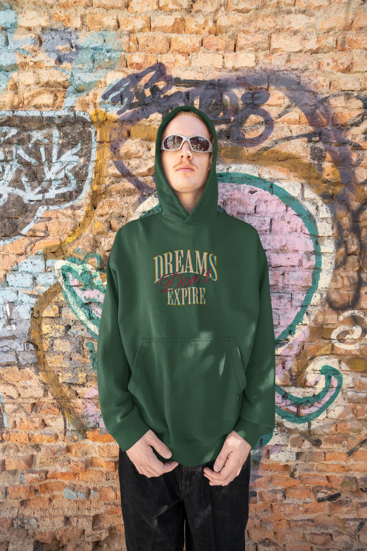 Person wearing a green hoodie with text against a graffiti-covered wall.