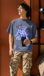 Person wearing a blue t-shirt with graphic design and text, standing against an orange wall.