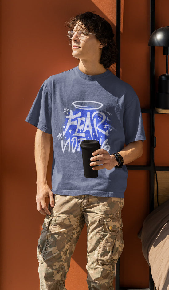 Person wearing a blue t-shirt with graphic design and text, standing against an orange wall.