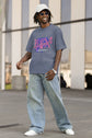 Person wearing a gray t-shirt with colorful design and blue jeans standing outdoors.