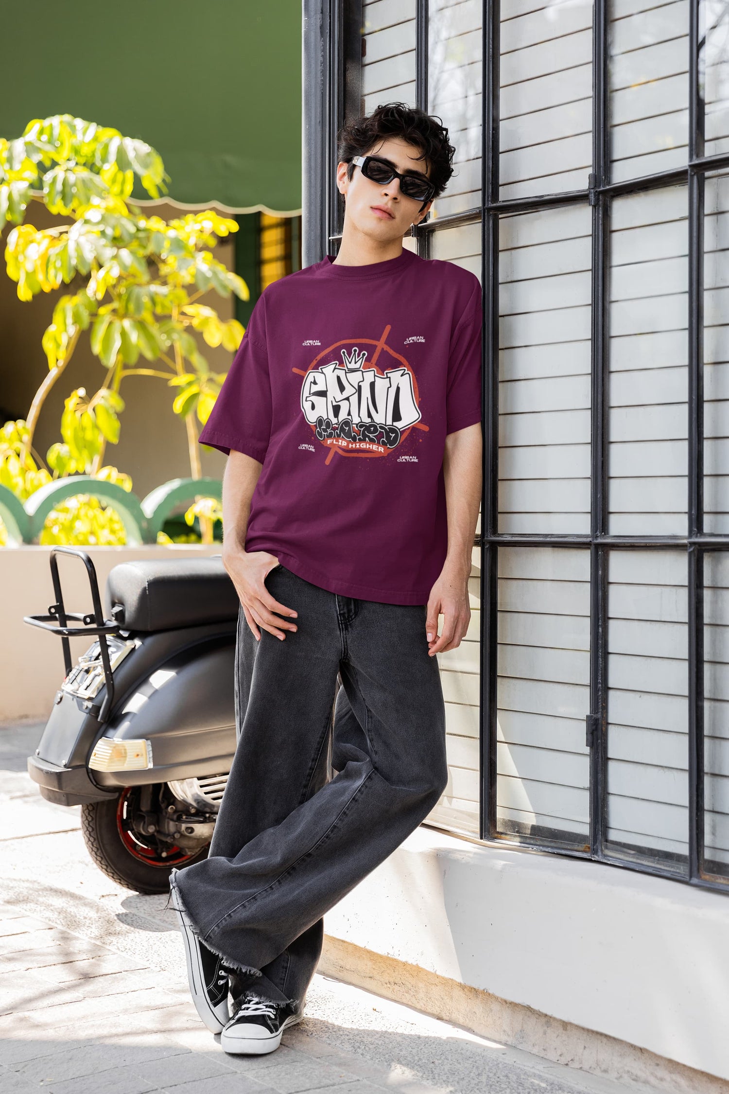 Person wearing a maroon t-shirt with a graphic design, standing outdoors near a scooter.