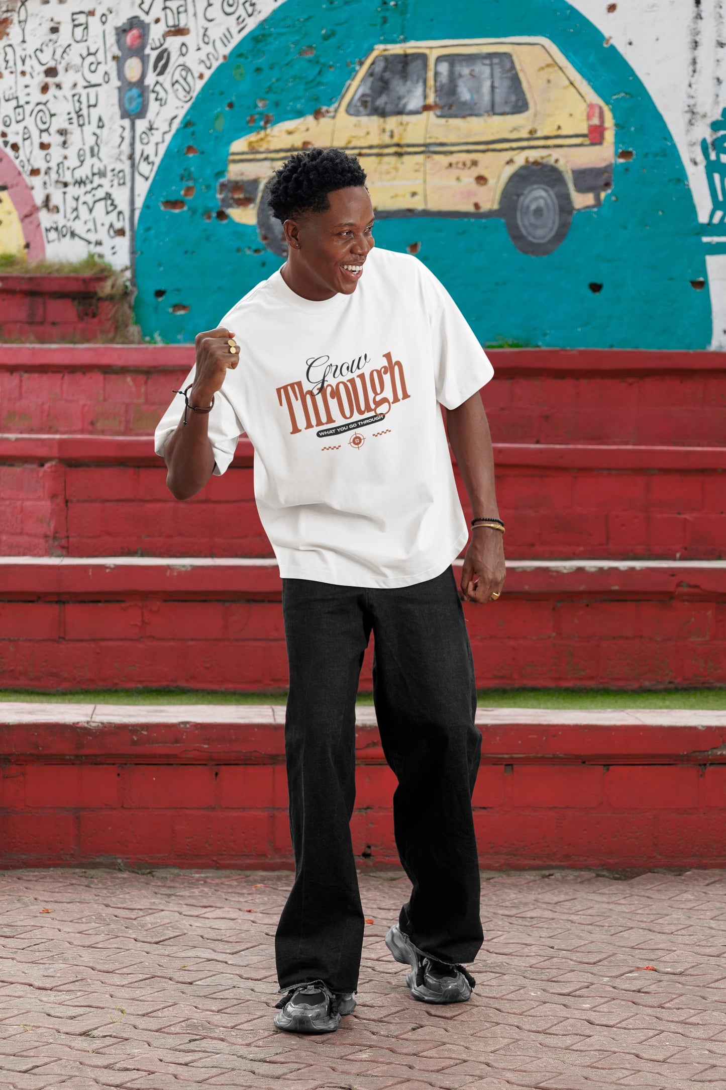 Person wearing a white t-shirt with text, standing in front of a colorful mural.
