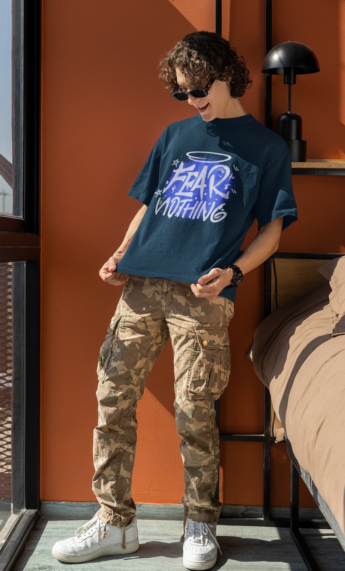 Person wearing a blue graphic t-shirt and camouflage pants standing indoors.