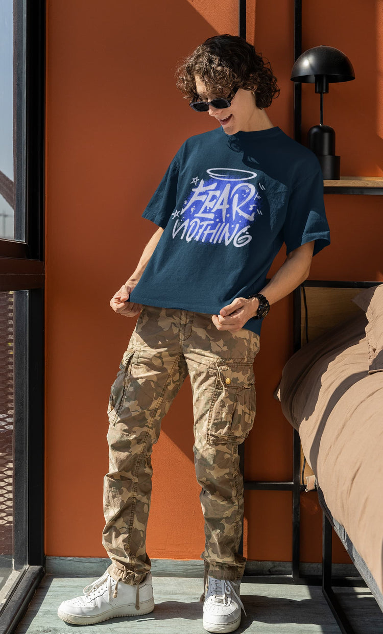 Person wearing a blue graphic t-shirt and camouflage pants standing indoors.