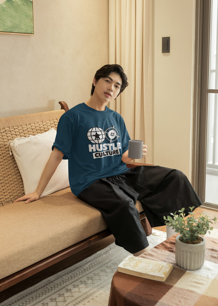 Person sitting on a couch wearing a blue t-shirt with text, holding a mug in a living room.