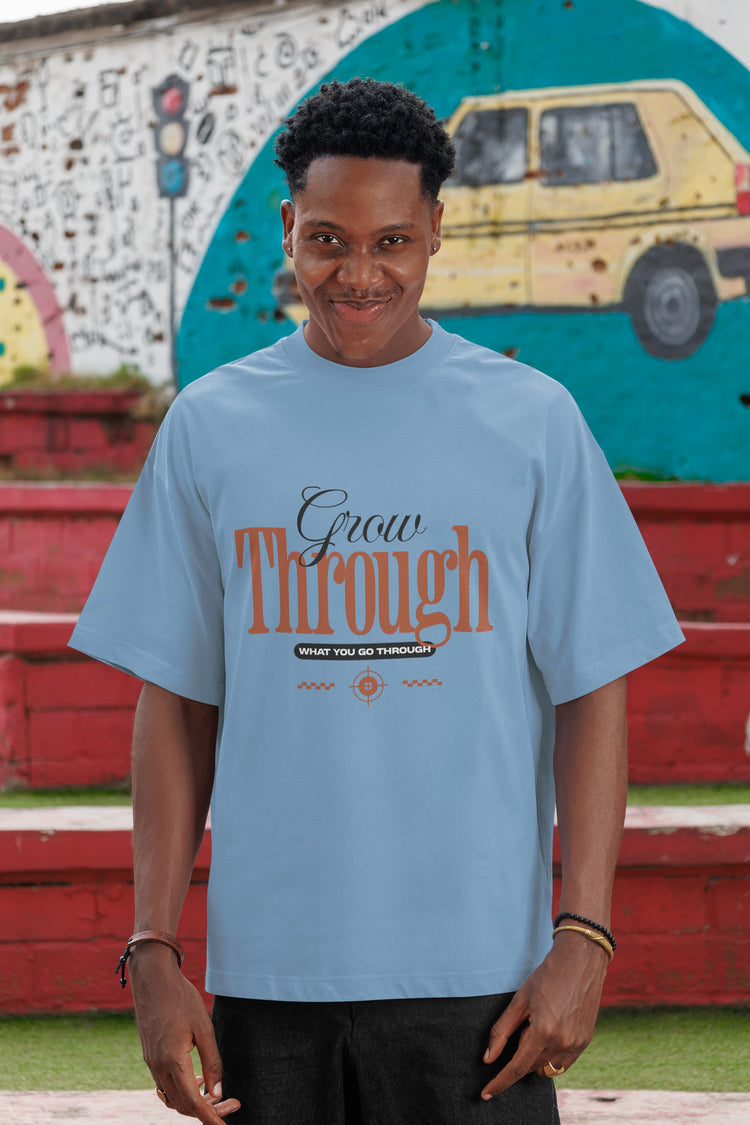 Person wearing a light blue t-shirt with text, standing in front of a colorful mural.