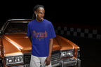 Man wearing a blue t-shirt with 'Through' printed on it, standing next to a classic car.