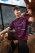 Person wearing a purple t-shirt with text and graphics, sitting on a wooden deck.