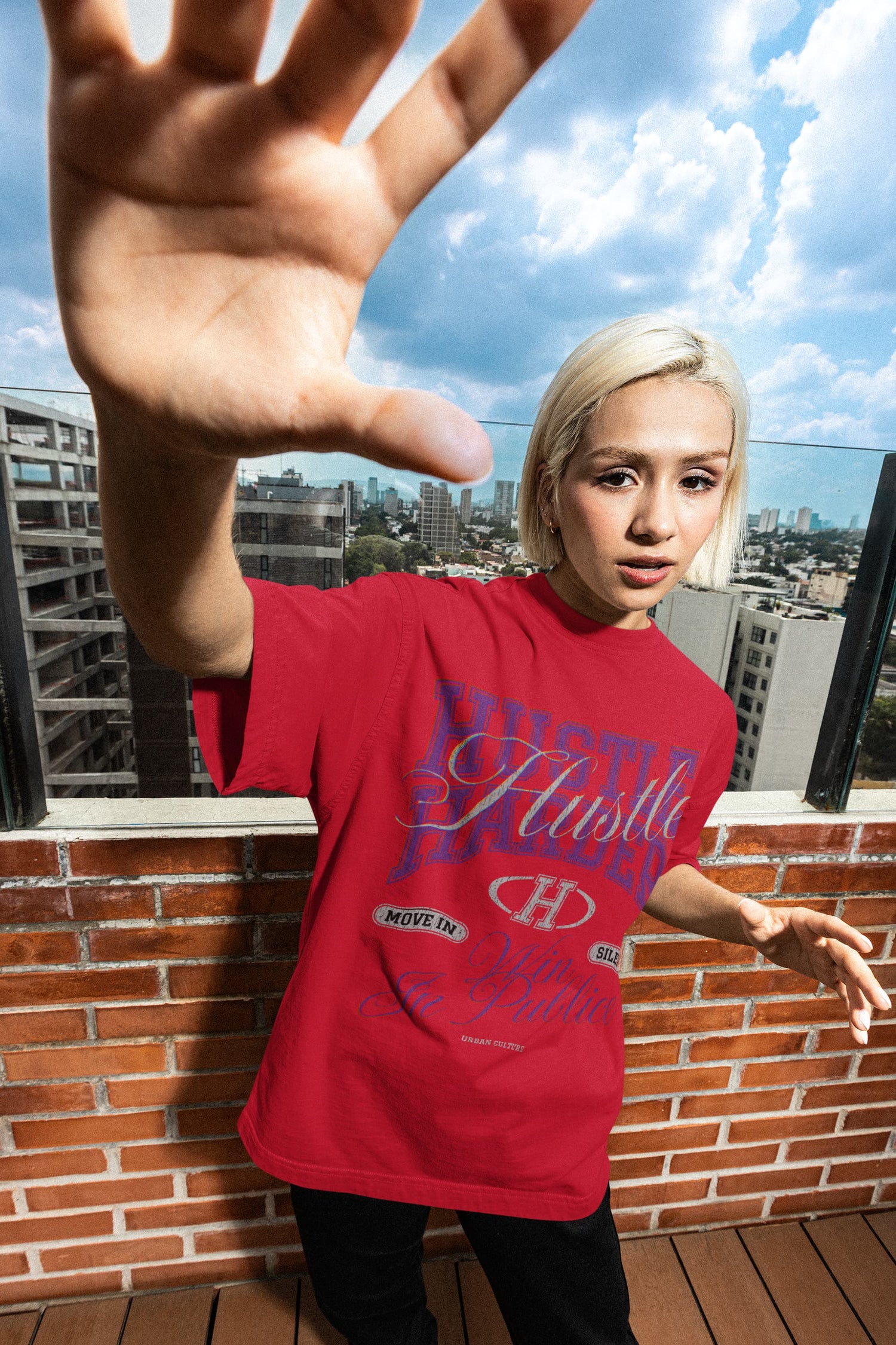 Person wearing a red t-shirt with visible branding, standing on a rooftop with cityscape in the background.