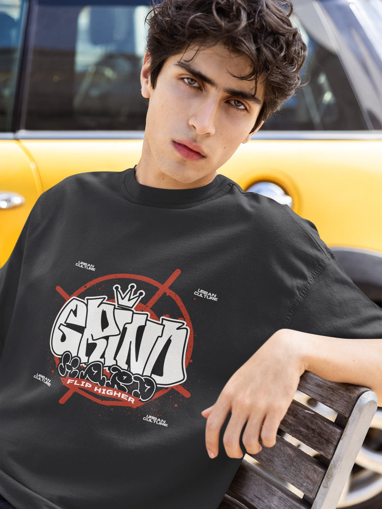 Person wearing a black t-shirt with graphic design, sitting on a bench with a yellow vehicle in the background.
