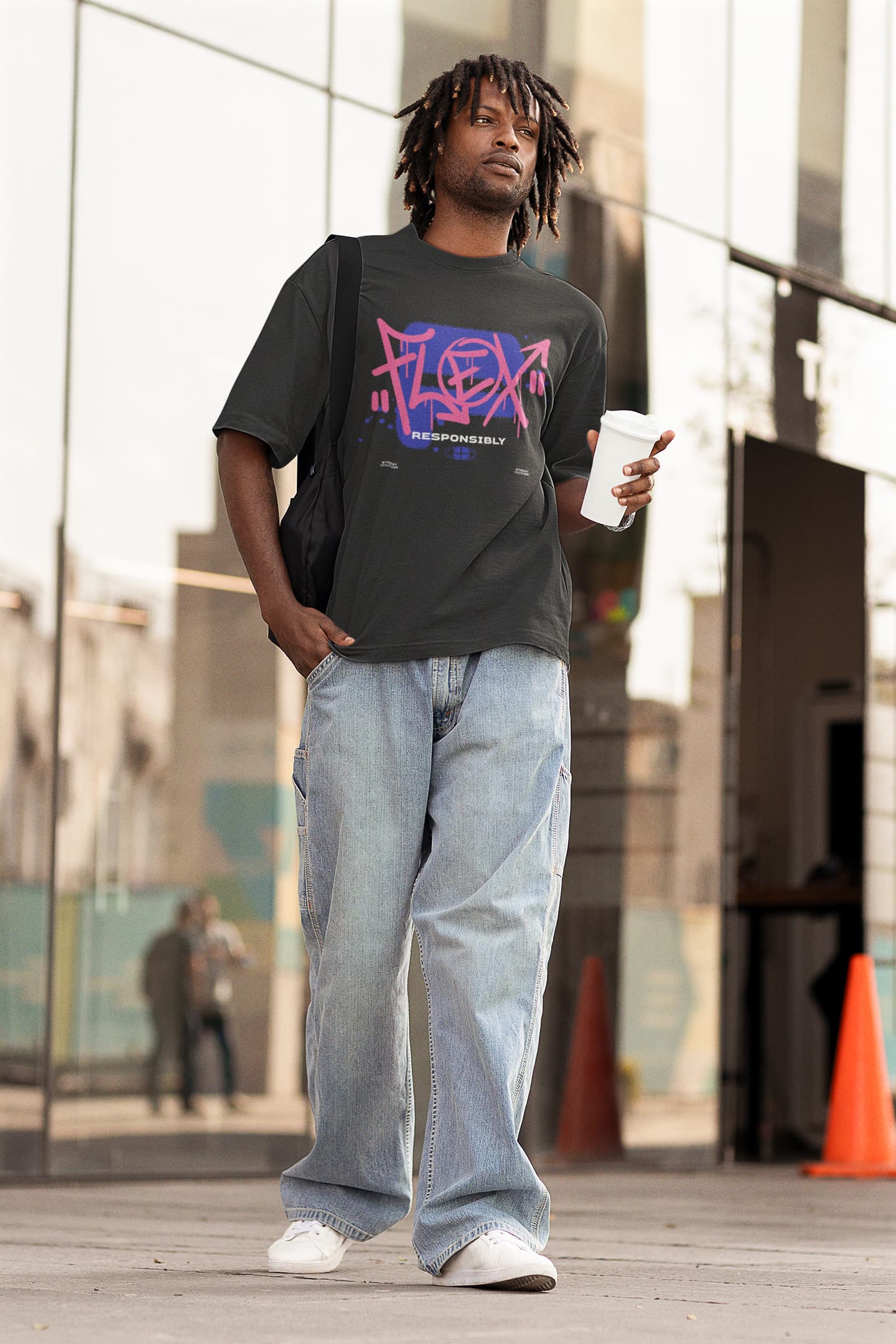 Man wearing a black t-shirt with 'FLEX' graphic, light blue jeans, and white sneakers, holding a cup outdoors.