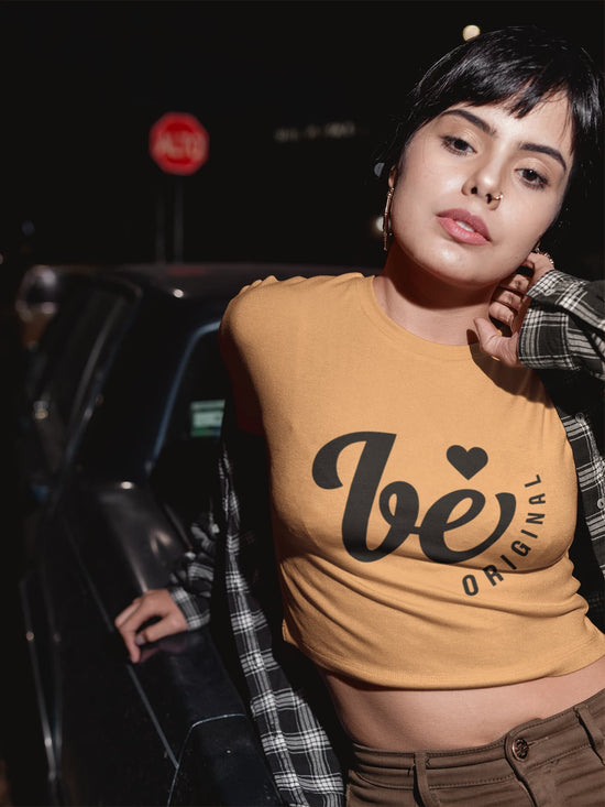 Woman wearing a mustard yellow shirt with text, standing outdoors at night.