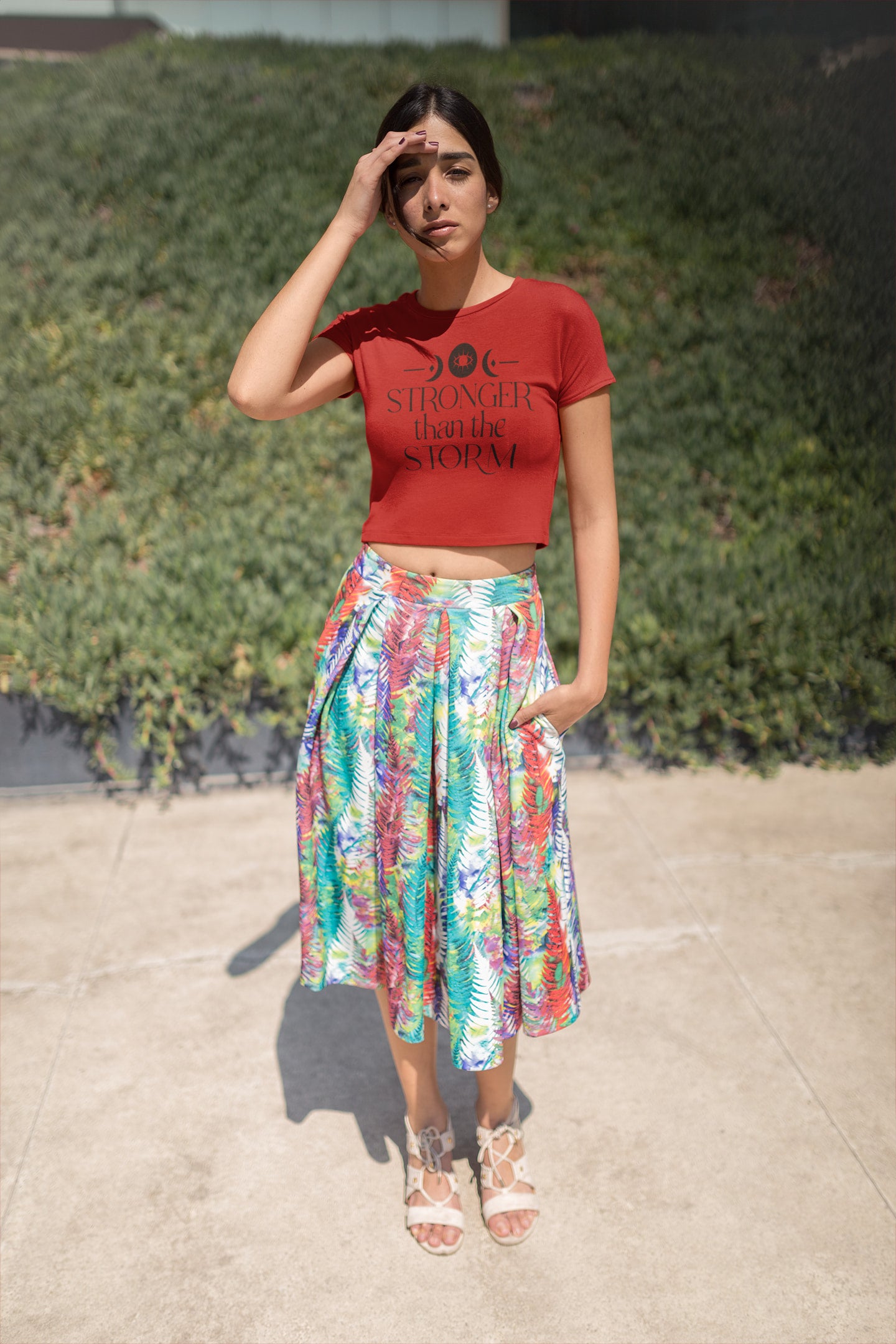 Woman wearing a red crop top and colorful skirt standing outdoors.