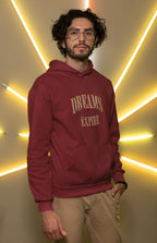 Man wearing a maroon hoodie with 'Dreams Don't Expire' text against a yellow neon light background