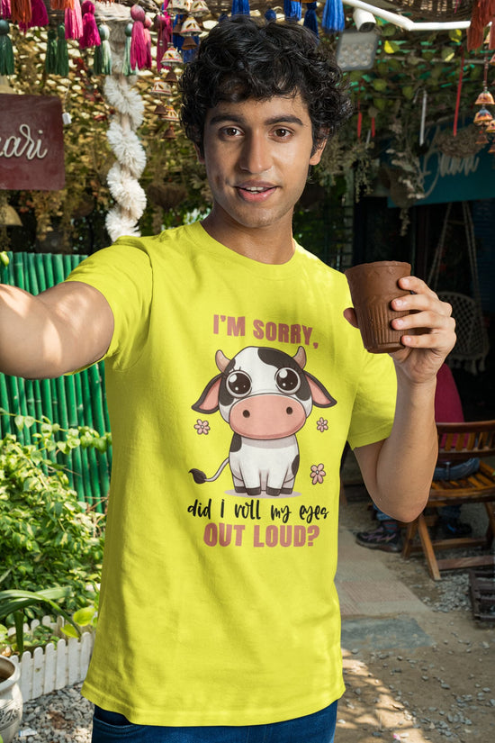 Person wearing a yellow t-shirt with a cow graphic and text, holding a cup outdoors.