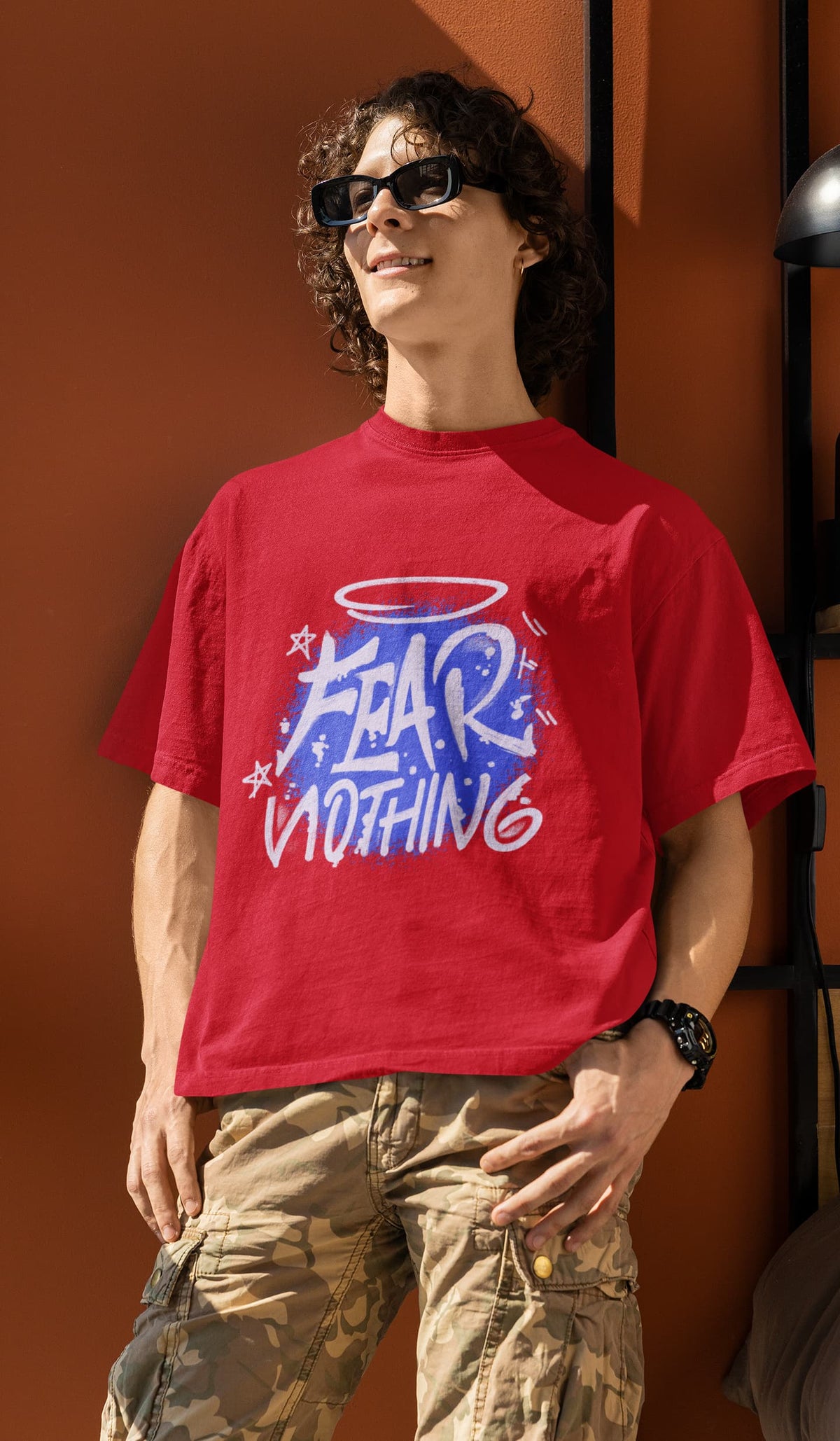 Person wearing a red t-shirt with graphic design and text, standing against an orange wall.