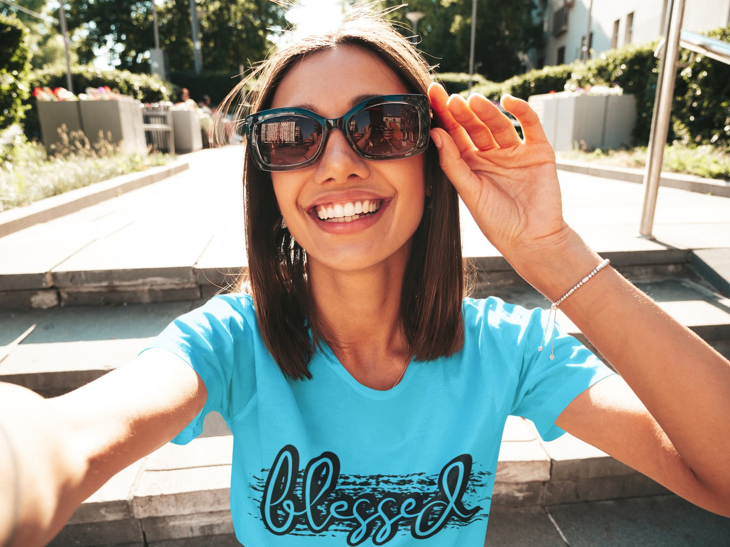 Woman wearing sunglasses and a blue t-shirt with 'blessed' on it, outdoors.
